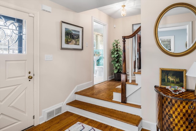 foyer featuring wood finished floors, visible vents, baseboards, and stairs