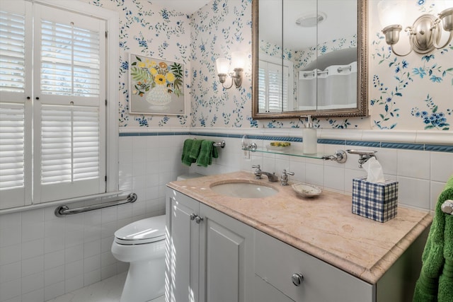 bathroom with toilet, wallpapered walls, a wainscoted wall, and vanity