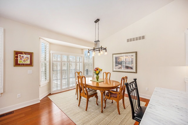 dining space with visible vents, vaulted ceiling, and wood finished floors