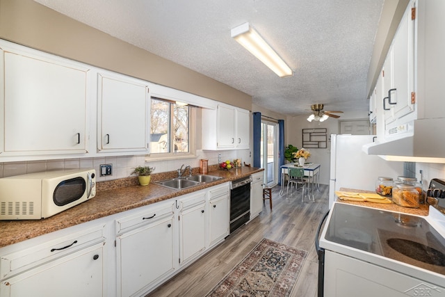 kitchen featuring dark countertops, light wood-style floors, white cabinetry, a sink, and white appliances