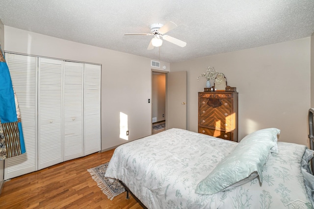 bedroom with ceiling fan, a textured ceiling, visible vents, and wood finished floors