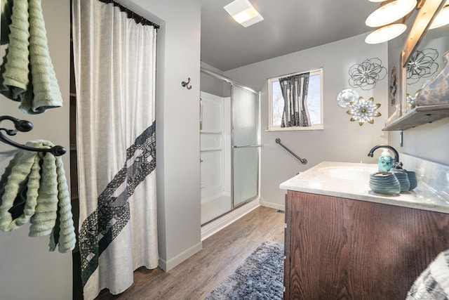 bathroom with a stall shower, wood finished floors, vanity, and baseboards