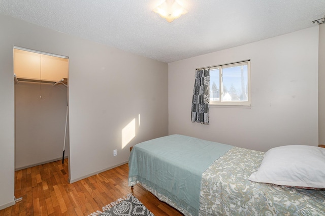 bedroom with attic access, a walk in closet, a textured ceiling, and wood finished floors