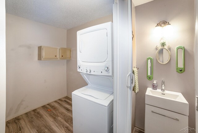 laundry room featuring laundry area, stacked washer / dryer, a textured ceiling, light wood-type flooring, and a sink