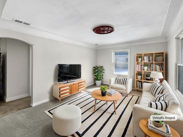 living area with arched walkways, light colored carpet, visible vents, and baseboards