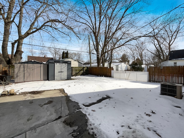 yard covered in snow with an outbuilding, central AC, a fenced backyard, and a shed