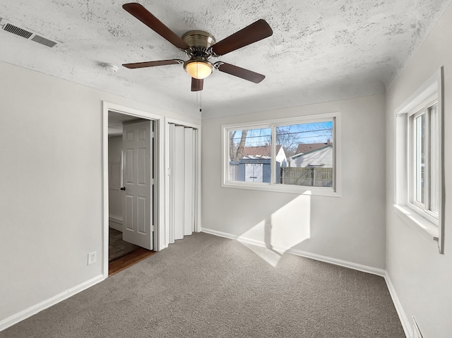 unfurnished bedroom featuring dark colored carpet, visible vents, ceiling fan, a textured ceiling, and baseboards