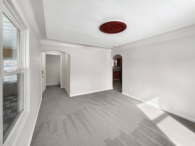 carpeted spare room featuring arched walkways and baseboards