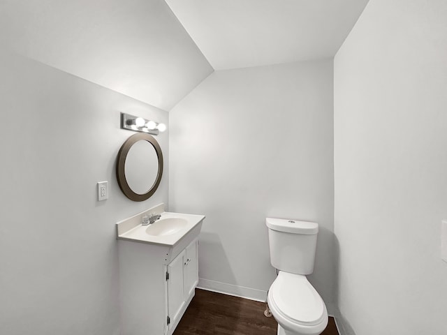 half bath featuring toilet, wood finished floors, vanity, baseboards, and vaulted ceiling