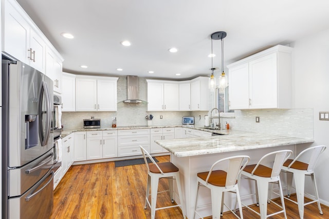 kitchen with stainless steel appliances, white cabinetry, a sink, a peninsula, and wall chimney exhaust hood