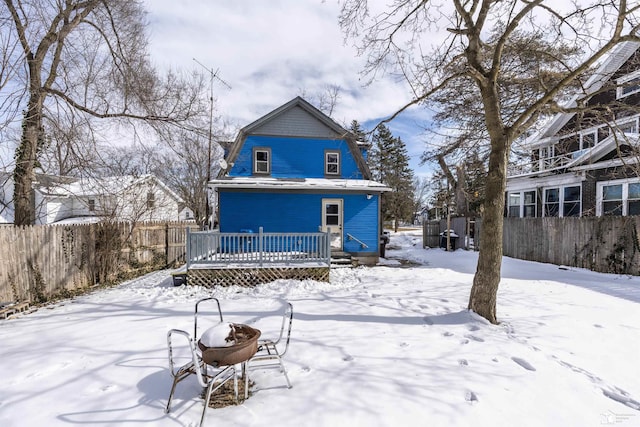 snow covered back of property with a fire pit, a wooden deck, fence, and a gambrel roof