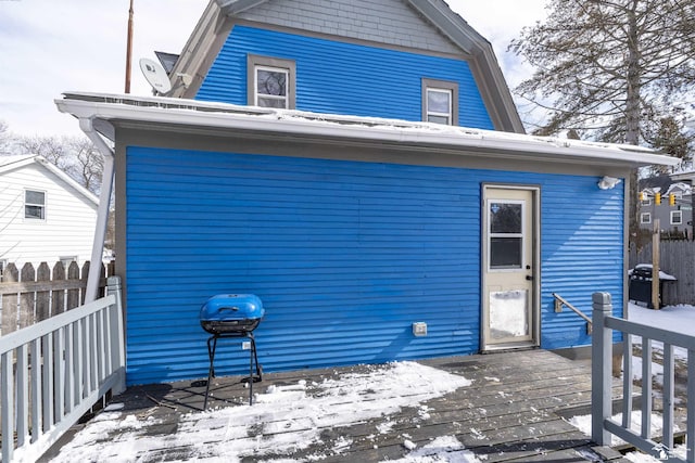 snow covered house featuring a wooden deck, fence, and a gambrel roof