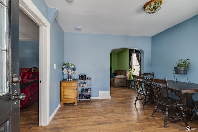 dining space with arched walkways, wood finished floors, visible vents, and baseboards