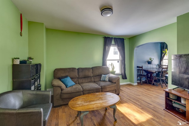 living room with arched walkways, light wood-style flooring, and baseboards