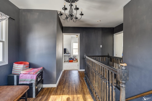 corridor with a notable chandelier, baseboards, dark wood-style flooring, and an upstairs landing