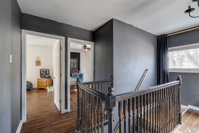 corridor featuring dark wood-style floors, baseboards, and an upstairs landing