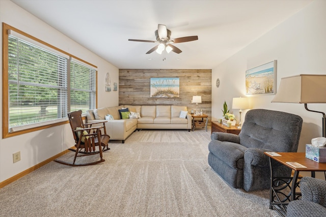 living area featuring light colored carpet, an accent wall, wood walls, ceiling fan, and baseboards