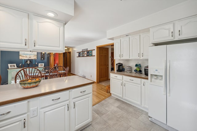 kitchen featuring white fridge with ice dispenser, light countertops, and white cabinets