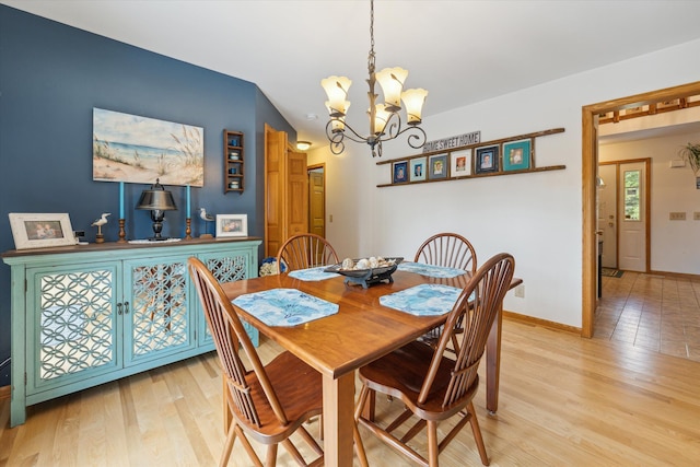 dining area featuring light wood-type flooring, baseboards, vaulted ceiling, and a notable chandelier