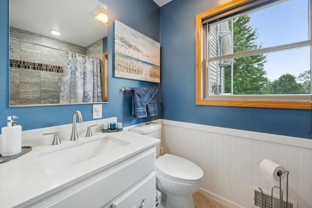 full bath with toilet, vanity, tiled shower, and wainscoting