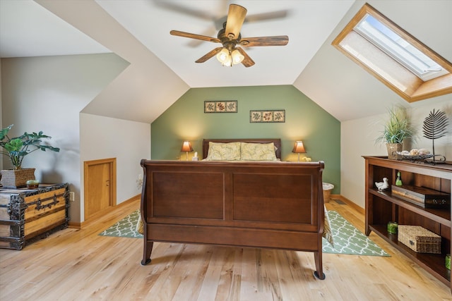 bedroom with vaulted ceiling with skylight, light wood finished floors, a ceiling fan, and baseboards