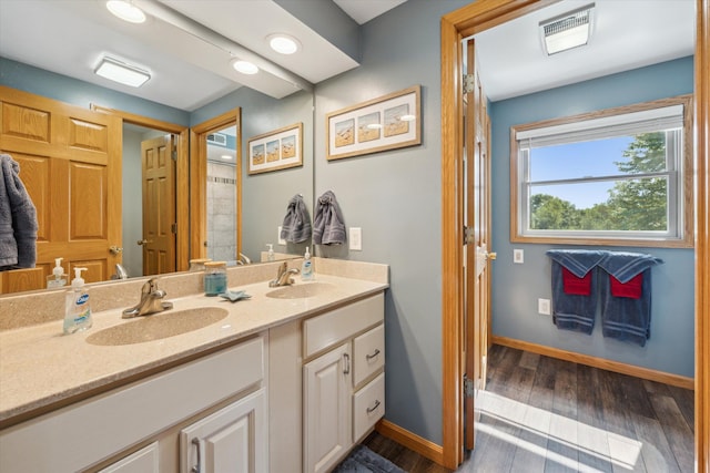 full bath with double vanity, visible vents, a sink, and wood finished floors