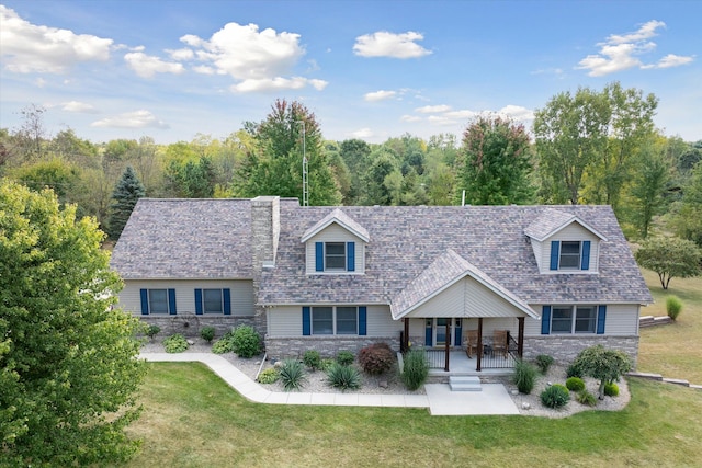 cape cod-style house featuring stone siding, a shingled roof, a porch, and a front yard