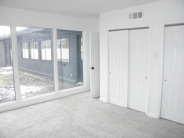 unfurnished bedroom featuring multiple closets, carpet flooring, visible vents, and baseboards