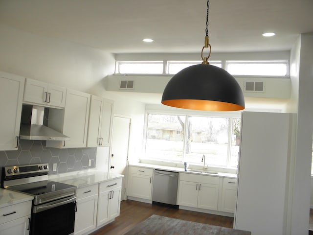 kitchen with stainless steel appliances, a sink, visible vents, backsplash, and wall chimney exhaust hood