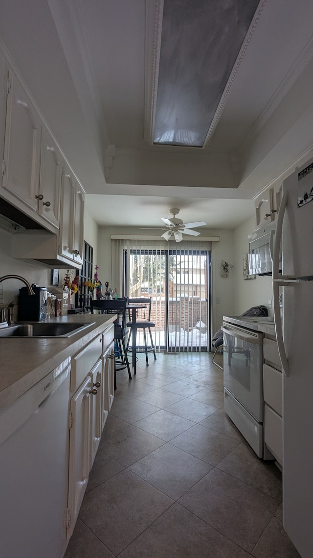 kitchen featuring a sink, a tray ceiling, white appliances, and white cabinetry