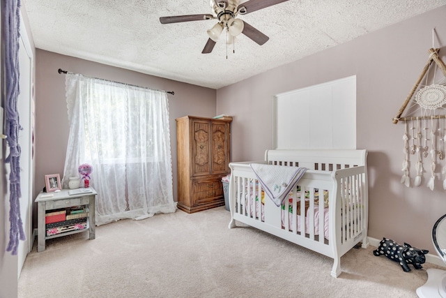 bedroom with a ceiling fan, carpet flooring, a textured ceiling, and a crib