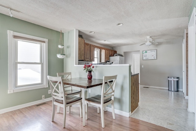 dining area featuring light wood finished floors, visible vents, baseboards, ceiling fan, and a textured ceiling