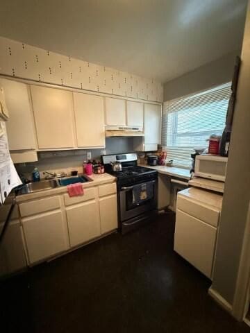 kitchen with light countertops, white microwave, white cabinets, a sink, and stainless steel gas range