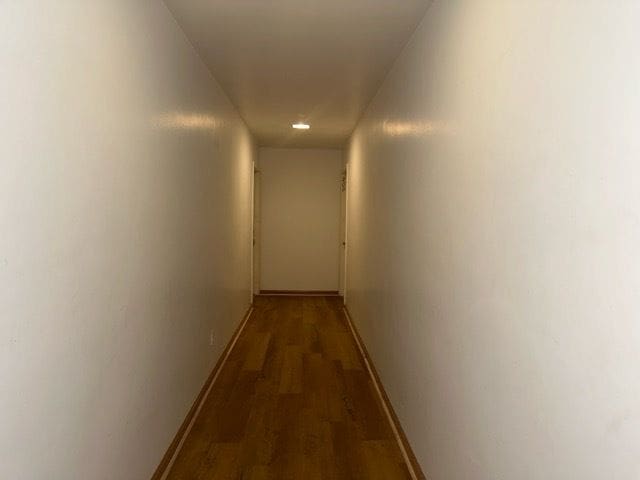 corridor with dark wood-style floors and baseboards