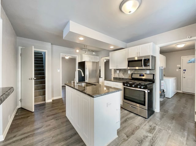 kitchen with a center island with sink, appliances with stainless steel finishes, dark stone countertops, white cabinetry, and a sink