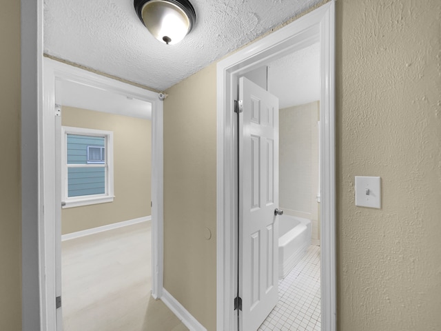 hallway featuring a textured wall, a textured ceiling, baseboards, and light tile patterned floors