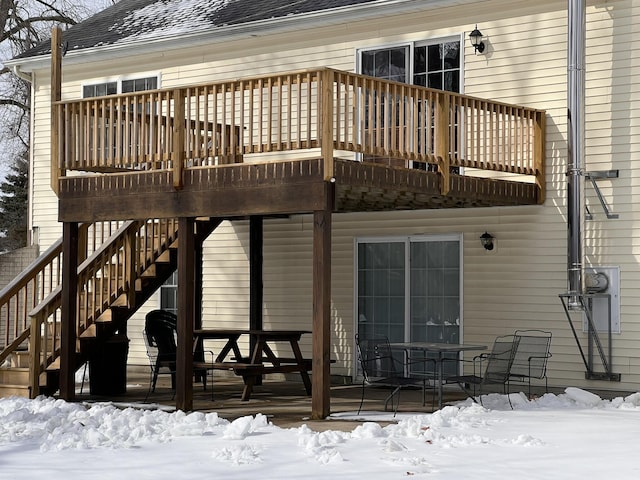 snow covered back of property with stairs, a deck, and roof with shingles