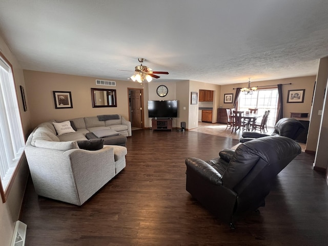 living area featuring a textured ceiling, ceiling fan with notable chandelier, dark wood finished floors, and visible vents