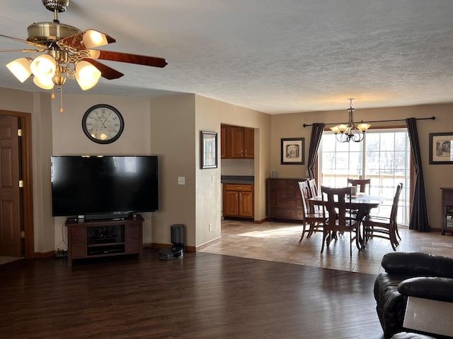 living area featuring a textured ceiling, light wood finished floors, ceiling fan with notable chandelier, and baseboards