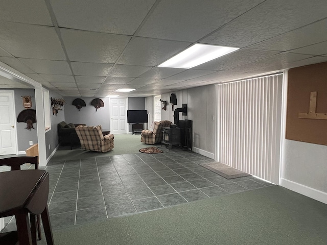 finished below grade area featuring a wood stove, a drop ceiling, dark tile patterned floors, and baseboards