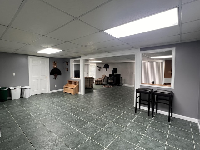 finished basement featuring dark tile patterned flooring, a drop ceiling, a wood stove, and baseboards