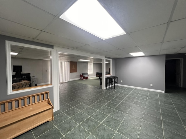 finished below grade area with a paneled ceiling, dark tile patterned flooring, and baseboards