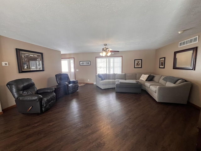 living area featuring a textured ceiling, dark wood-type flooring, visible vents, and baseboards