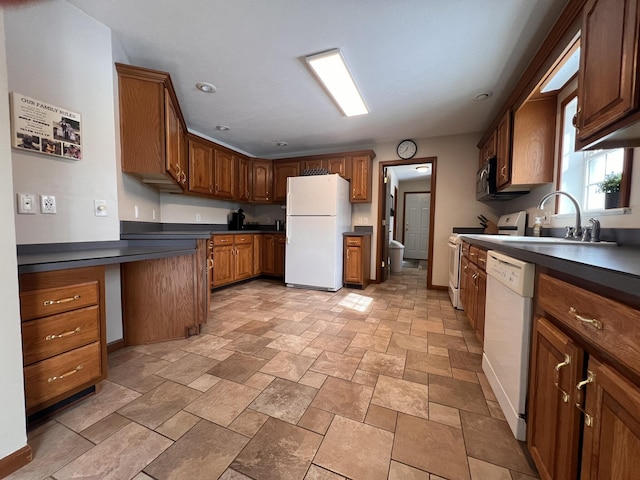 kitchen featuring white appliances, a sink, baseboards, brown cabinetry, and dark countertops