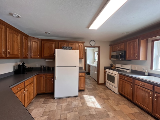 kitchen featuring white appliances, brown cabinetry, and dark countertops