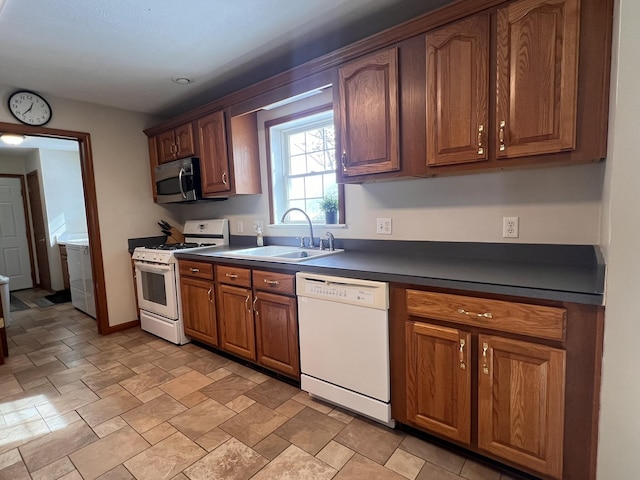 kitchen featuring brown cabinets, dark countertops, a sink, white appliances, and baseboards