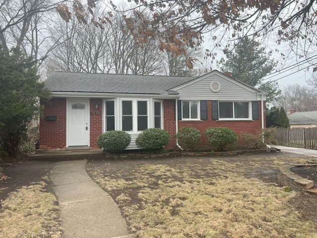 ranch-style house featuring roof with shingles, fence, and brick siding