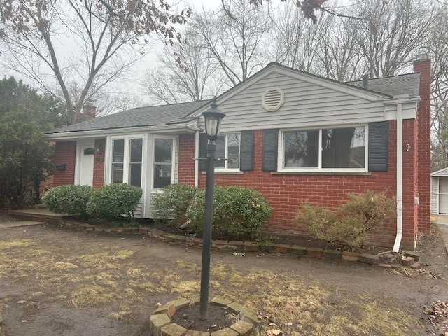 ranch-style home with brick siding, a chimney, and roof with shingles