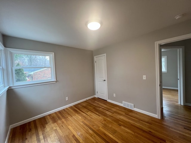 empty room featuring wood finished floors, visible vents, and baseboards