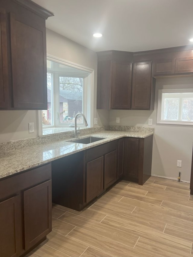 kitchen with dark brown cabinetry, light stone countertops, wood tiled floor, a sink, and recessed lighting